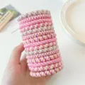 Macro view of fifteen braided pink high elasticity hair ties held by a hand on white - 15 Pieces/Pack / Pink Canister