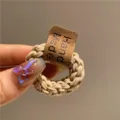 Gros plan d'un élastique à cheveux tressé beige avec étiquette en cuir cousue - Beige