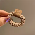 Gros plan détaillé d'un élastique à cheveux tressé beige avec un patch ours en cuir mignon - Café Clair