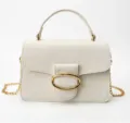 Detailed view of white pebbled leather handbag with gold oval buckle and chain strap - White