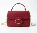 Elegant wine red pebbled leather handbag with gold oval buckle and chain strap detail. - Red