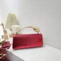 Close-up of elegant metallic red evening clutch bag with unique golden floral handle - Red