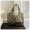 Λεπτομερής προβολή της κομψής διαφανούς τσάντας PVC σε γκρι χρώμα με λευκό κείμενο - Καφέ