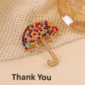 Close-up of retro golden umbrella brooch featuring colorful rhinestones and pearl details. - Colorful Umbrella