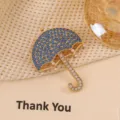 Detailed view of a vintage umbrella brooch featuring blue rhinestones and white pearls - Blue Umbrella