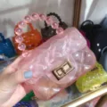 Close-up detail of a pink mini quilted jelly handbag featuring a beaded handle and gold lock - Transparent Pink