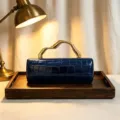 Elegant navy blue crocodile-patterned evening clutch with a unique gold sculptural handle. - Blue
