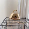 Close-up detail of a reflective gold acrylic evening bag with a metallic top handle - Gold
