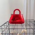 Close-up detail of a glossy red acrylic evening bag featuring gold chain strap - Red