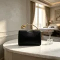 Detail view of an elegant black evening clutch bag with a golden rose flower branch handle. - Black