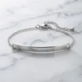 Detailed close-up of polished stainless steel curved bar bracelet on white marble surface - Silver