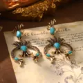 Gros plan macro de boucles d'oreilles dorées style palais français avec turquoises - Style Géométrique à Franges (23135A-6000)