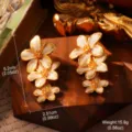 Gros plan d'élégantes boucles d'oreilles fleurs en émail blanc de style français doré. - Style de Goutte de Fleur Triple (2-25677C-9500)
