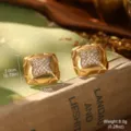 Vue macro de boucles d'oreilles carrées vintage en or avec cristaux sur un vieux livre - Or Carré (2-28265-5600)