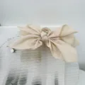 Detailed view of a large beige fabric bow hair claw clip on a modern display stand - Beige