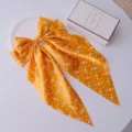 Detailed view of yellow polka dot bow hair clip with long ribbons on white surface - Yellow Polka Dot