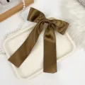 Close-up of a premium brown satin bow hair clip with long ribbons on a elegant white tray - Brown