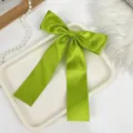 Close-up of lime green satin bow hair clip with long ribbon streamers for hair styling - Green