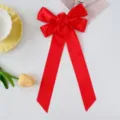 Close-up detail of a red ribbon bow hair clip with center rose and long streamers. - Red