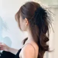 Elegant black ostrich feather hair claw clip for a stylish side ponytail hairstyle detail. - Black