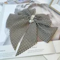 Close-up of a vintage houndstooth bow hair clip with elegant pearl detailing on a magazine - Dark Brown Houndstooth