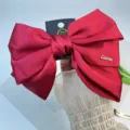 Primer plano de un lazo para el pelo de satén rojo de tres capas con placa metálica dorada. - Estilo Con Letras Inglesas / Rojo