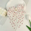 Gros plan sur le nœud en mousseline de soie plissée blanche à pois rouges et perles - Rouge Corail