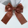 Macro shot of a shimmering brown satin ribbon bow hair clip on a minimal white background - Coffee