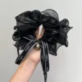 Macro detail of a black mesh hair scrunchie featuring a ribbon bow and pearl accessory. - Pearl Bow Scrunchie / Black