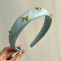 Detail view of a light blue satin padded headband with gold-toned metal bow charms. - Blue With 7 Bows