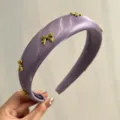 Detailed view of a purple satin padded headband featuring elegant gold bow charm accents. - Purple With 7 Bows