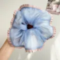 Close-up van een blauwe mesh scrunchie met roze geplooide randen en fijne textuur. - Blauw