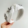 Close-up detail of white knotted headband with silver metal flower ornaments - 金属花挂件打结发箍 / White