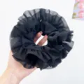 Detail of a large black ruffle mesh scrunchie held in hand to show size and texture. - Black