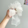 Detailansicht eines weißen, schimmernden Organza-Haargummis mit Schleife in der Hand. - Haargummis aus Netzstoff mit Schleife / Gebrochenes Weiß