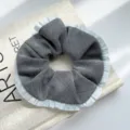 Detaillierte Nahaufnahme eines grauen Haargummis mit hellblauen Rüschenkanten für Damen - Haargummi / Plissierter Rand Scrunchie