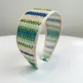 Gros plan sur la texture tissée et les rayures colorées de ce serre-tête large pour femme. - Vert