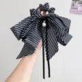 Nahaufnahme eines gestreiften Schleifen-Haargummis mit Perle in der Hand. - Perle Schleife Band Scrunchie / Schwarz-weiße Streifen