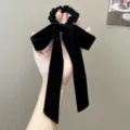 Detail view of an elegant black velvet bow scrunchie featuring long hanging ribbons - Bow Streamer Style / Black
