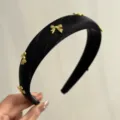 Detailed view of a thick black satin headband featuring small decorative golden metal bows. - Black With 7 Bows