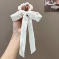 Close-up view of a luxury off-white velvet bow scrunchie with long streamers held by hand - Bow Streamer Style / White