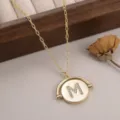 Détail d'un collier doré avec pendentif circulaire rotatif orné d'une lettre M en strass. - 镶钻字母M款