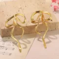 Close-up of golden metal bow earrings with flowing geometric lines on stone - Polished Gold Ribbon Bowknot Stud Style (2-27272-9000)