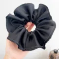 Gedetailleerde weergave van een grote zwarte geplooide haarelastiek met gerafelde randen. - Scrunchie / Zwart