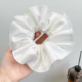 Close-up van een grote witte geplooide satijnen scrunchie met delicate golvende randen. - Scrunchie / Wit