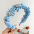 Detailansicht eines hellblauen Rüschenstirnbandes mit silbernen Rosenornamenten. - Blau