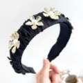 Close-up of elegant pleated black headband with golden metal flowers and pearls - Black