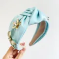 Gros plan d'un serre-tête en satin bleu clair orné de fleurs en métal doré et de cristaux. - Serre-tête Noué avec Fleur 3D en Strass / Bleu