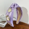 Detailed shot of purple satin knotted headband with gold metal flower and pearl decor. - Knotted Flower Headband / Purple
