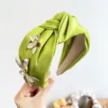 Gros plan d'un serre-tête en satin vert noué avec détails de fleurs en métal et cristaux - Serre-tête Noué avec Fleur 3D en Strass / Vert